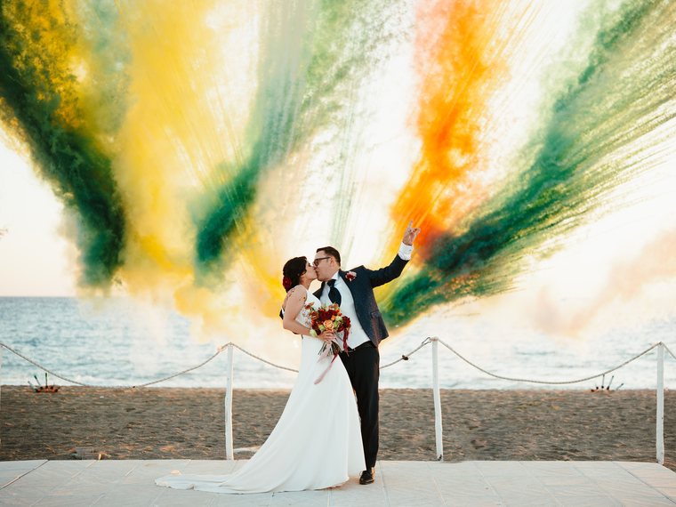 Fumigènes de couleur déployés derrière un couple de mariés sur une plage